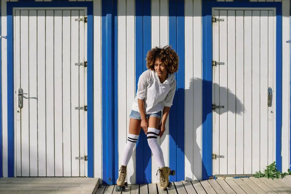 Ung svart kvinna på rullskridskor nära en strandhydda. — Stockfoto