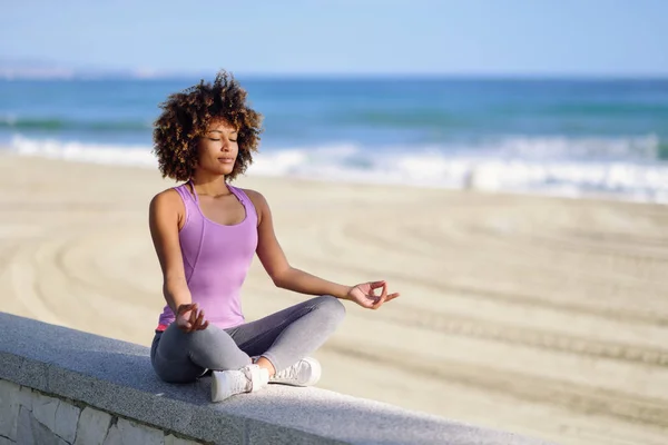 Black woman, afro hairstyle, in lotus pose with eyes closed in the beach — Stock Photo, Image