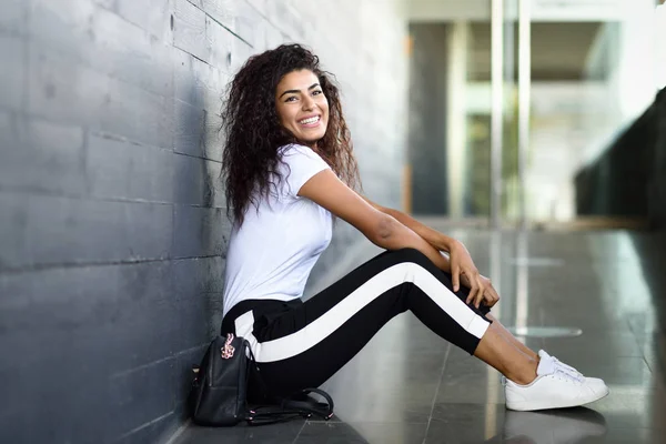 Happy African woman with black curly hairstyle sitting on urban floor. — Stock Photo, Image