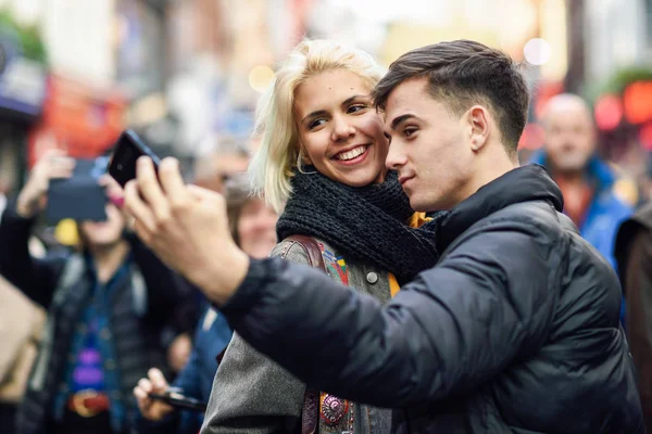 Couple heureux de touristes prenant selfie dans une rue bondée . — Photo