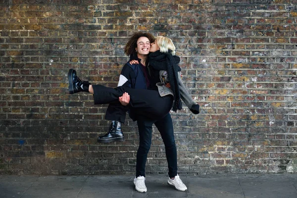 Man holding his girlfriend in his arms in front of a brick wall typical of London — Stock Photo, Image