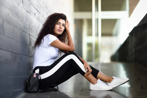 Afrikaanse vrouw met zwart krullend kapsel zittend op de stedelijke vloer. — Stockfoto