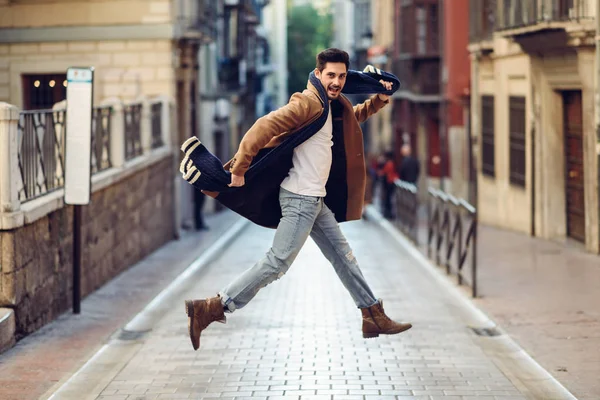 Joven hombre feliz saltando con ropa de invierno en el fondo urbano — Foto de Stock