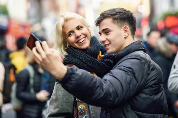 Szczęśliwa para turystów biorąc selfie w zatłoczonej ulicy. — Zdjęcie stockowe