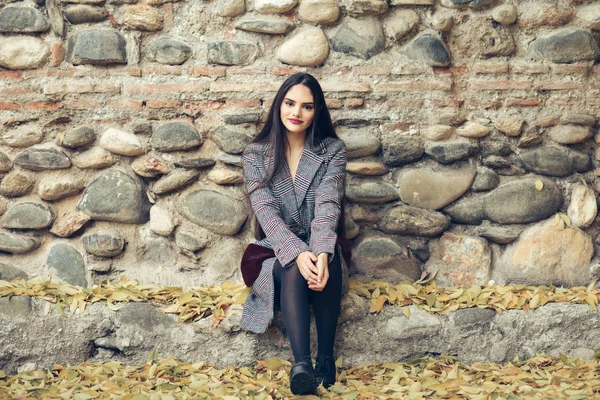 Chica joven con el pelo muy largo con abrigo de invierno sentado en el suelo lleno de hojas de otoño —  Fotos de Stock