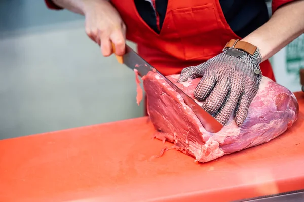 Kobieta krojenia świeżego mięsa w sklepie mięsnym z metalowymi rękawicami z siatki bezpieczeństwa — Zdjęcie stockowe