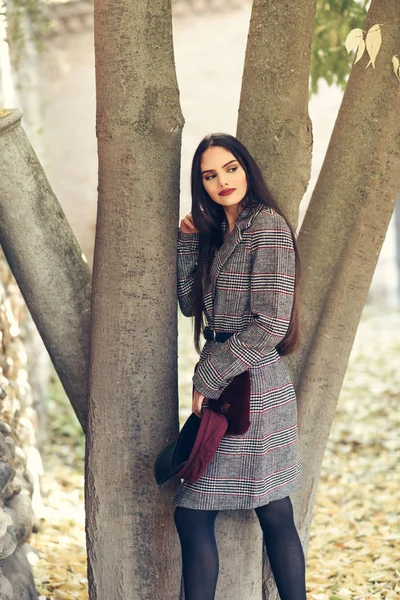 Chica con el pelo muy largo con abrigo de invierno y gorra en el parque urbano lleno de hojas de otoño —  Fotos de Stock