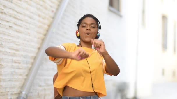 Молода чорна жінка слухає музику і танцює на вулиці . — стокове відео