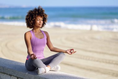 Siyah kadın, afro saç modeli, gözleri plajda kapalı lotus asana