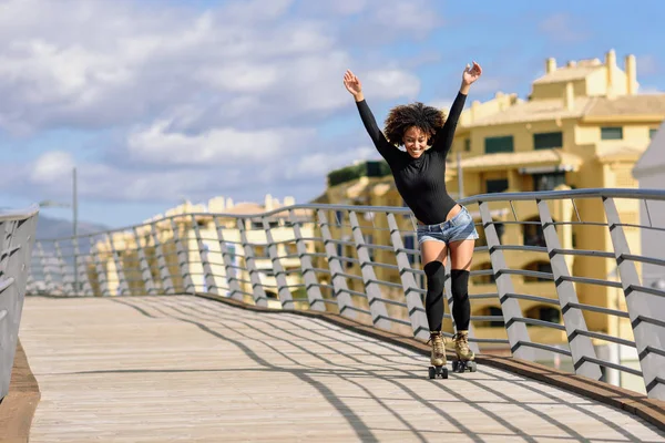 Afro acconciatura donna sui pattini a rotelle equitazione all'aperto sul ponte urbano — Foto Stock