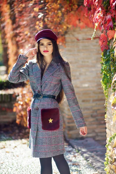 Joven hermosa chica con abrigo de invierno y gorra en el fondo de hojas de otoño. — Foto de Stock