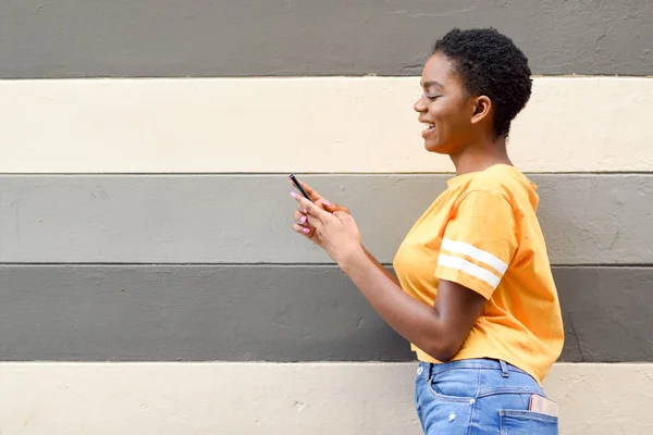 Černá dívka se usmívá a používá svůj elegantní telefon venku. — Stock fotografie