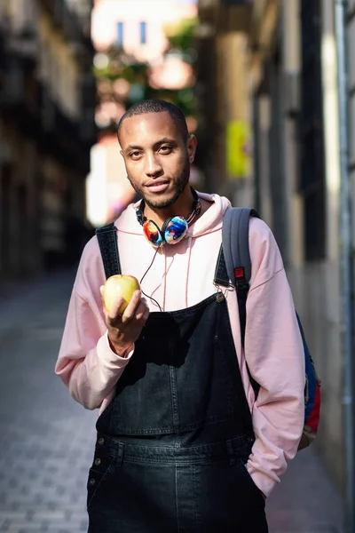 Young black man eating an apple walking down the street.