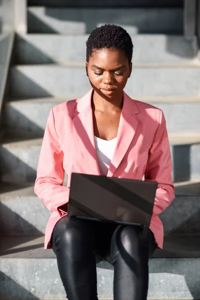 Zwarte vrouw zittend op stedelijke trappen werken met een laptop computer. — Stockfoto