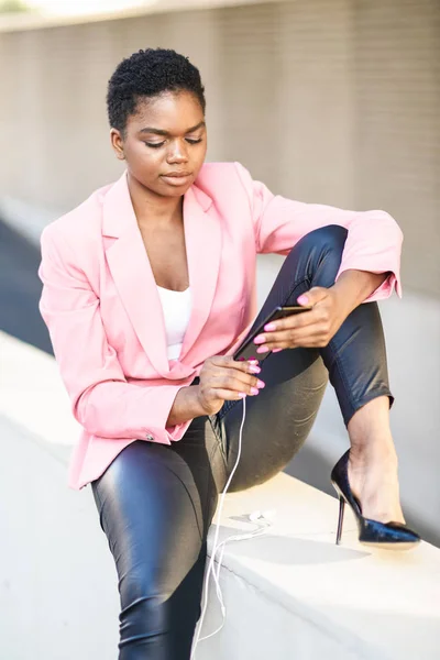 Empresaria negra sentada al aire libre usando smartphone con auriculares —  Fotos de Stock