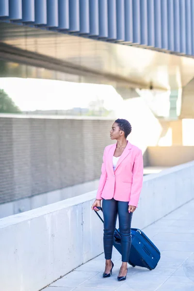 Zwarte vrouw wandelen met reistas dragen roze jasje. — Stockfoto