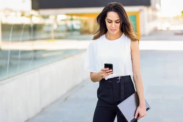 Femme d'affaires d'âge moyen travaillant avec son téléphone intelligent et son ordinateur portable à l'extérieur . — Photo