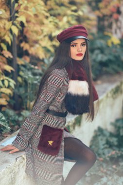 Uzun saçlı, sonbahar yapraklarında kışlık palto ve şapka giyen güzel bir kız.