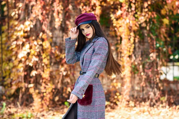 Joven hermosa chica con abrigo de invierno y gorra en el fondo de hojas de otoño. — Foto de Stock