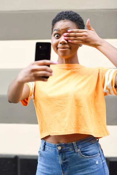 Mujer negra divertida tomando fotografías selfie con expresión feliz al aire libre —  Fotos de Stock