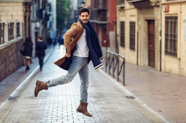 Genç mutlu adam kentsel arka planda kış giysileri giyen atlama