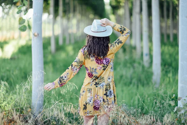 Young woman, wearing flowered dress, between trees. — Stock Photo, Image