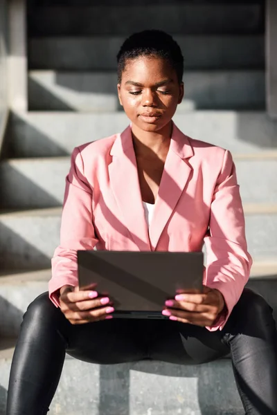 Μαύρη επιχειρηματίας που κάθεται σε αστικά σκαλοπάτια δουλεύοντας με φορητό υπολογιστή. — Φωτογραφία Αρχείου