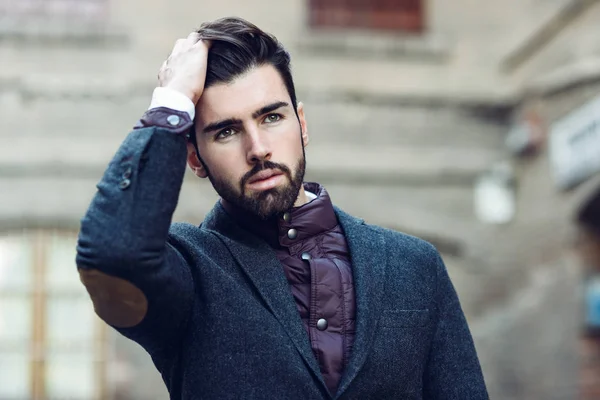 Young bearded man wearing british elegant suit touching his hair