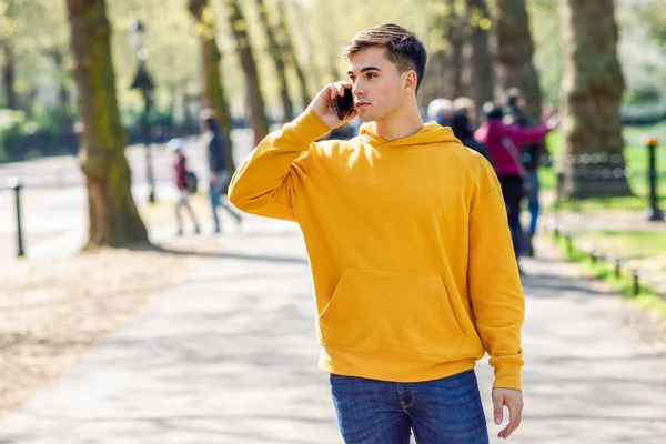 Joven hombre urbano usando smartphone caminando en la calle en un parque urbano en Londres . — Foto de Stock