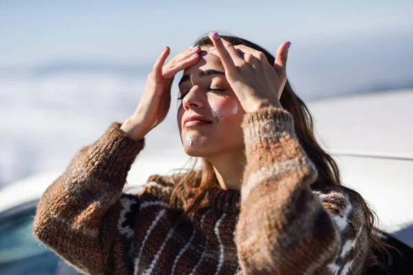 Giovane donna che applica la protezione solare sul suo viso nel paesaggio della neve — Foto Stock