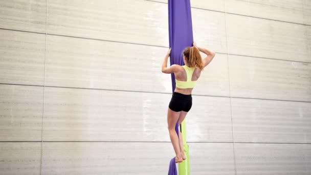 Jeune femme rousse faisant acrobatie gymnastique aérienne avec des tissus acrobatiques à l'intérieur d'une salle de gym . — Video