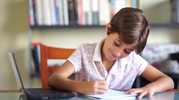 Niña haciendo deberes con un portátil y un cuaderno . — Vídeos de Stock