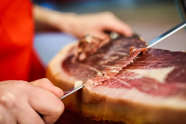 Professional cutter carving slices from a whole bone-in serrano ham — Stock Photo, Image