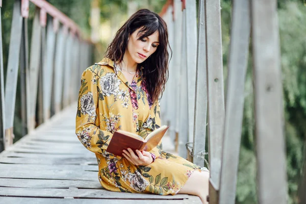 Mujer joven leyendo un libro sobre un puente rural . —  Fotos de Stock