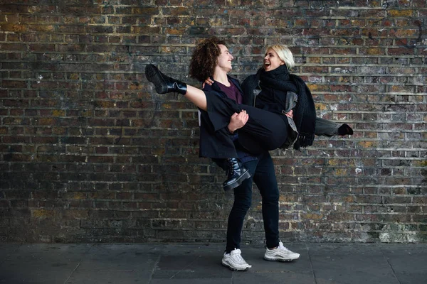 Man holding his girlfriend in his arms in front of a brick wall typical of London — Stock Photo, Image