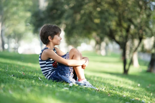 小さな女の子、8歳、屋外の草の上に座って. — ストック写真