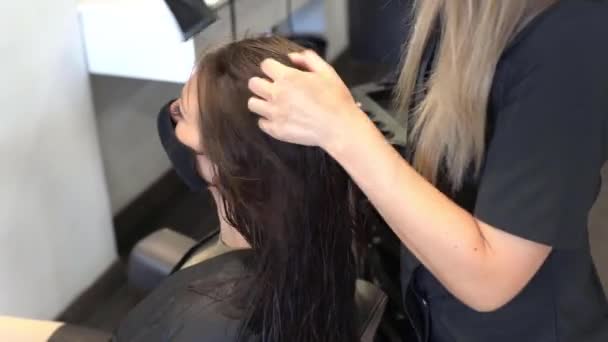 Kadeřník sušení její klientky vlasy s fénem na sobě ochranné masky v kosmetickém centru. — Stock video