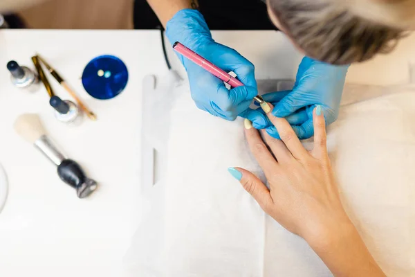 Gros plan de l'esthéticienne peignant ses clients ongles en vernis bleu et jaune. — Photo