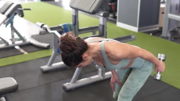 Женщина работает над трицепсами и бицепсами в спортзале с гантелями — стоковое видео
