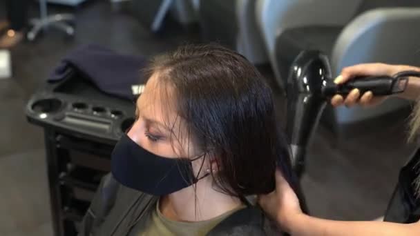 Kadeřník sušení její klientky vlasy s fénem na sobě ochranné masky v kosmetickém centru. — Stock video