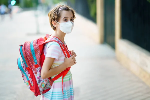 Девятилетняя девочка возвращается в школу в маске и школьной сумке. — стоковое фото