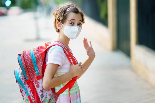 Девятилетняя девочка возвращается в школу в маске и школьной сумке. — стоковое фото