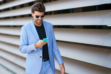 Adam mutlu bir ifadeyle akıllı telefonunu kullanarak sokakta yürüyor.