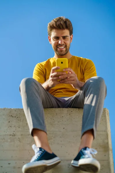 Hombre usando su teléfono inteligente sentado en una cornisa fuera — Foto de Stock