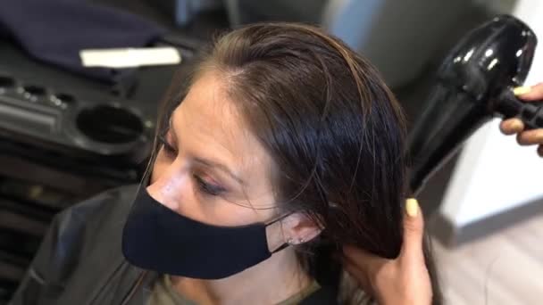 Frisör torkar sina kunder hår med en hårtork bär skyddande masker i ett skönhetscenter. — Stockvideo