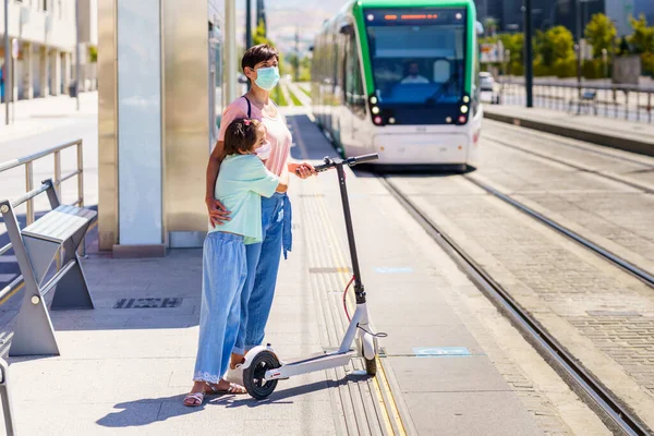 Madre e hija esperando el tren con un scooter electrónico. —  Fotos de Stock