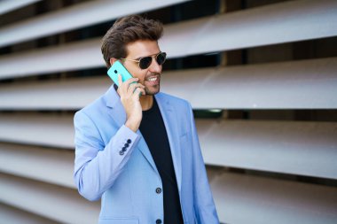 Adam mutlu bir ifadeyle akıllı telefonunu kullanarak sokakta yürüyor.