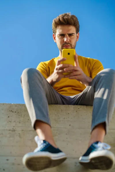 Hombre usando su teléfono inteligente sentado en una cornisa fuera — Foto de Stock