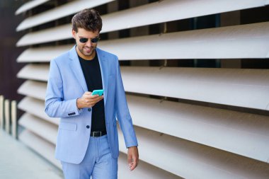 Adam mutlu bir ifadeyle akıllı telefonunu kullanarak sokakta yürüyor.