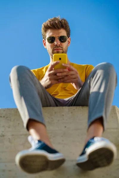 年轻人坐在外面的窗台上，用他的智能手机 — 图库照片